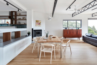Inspiration for a mid-sized contemporary kitchen/dining combo in Melbourne with white walls, light hardwood floors, a wood stove, brown floor, a concrete fireplace surround and exposed beam.