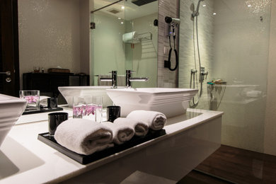 Large trendy master gray tile and porcelain tile cement tile floor, brown floor and double-sink bathroom photo in Los Angeles with white cabinets, a wall-mount toilet, beige walls, a wall-mount sink, solid surface countertops, white countertops and a floating vanity