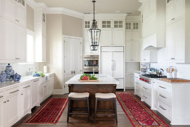 This is an example of a large traditional u-shaped kitchen in Dallas with a farmhouse sink, shaker cabinets, white cabinets, white splashback, panelled appliances, dark hardwood floors, with island, brown floor and white benchtop.