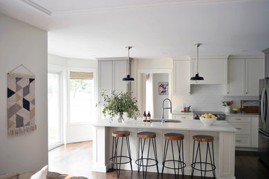 Example of a large transitional dark wood floor and brown floor kitchen design in Calgary with a double-bowl sink, shaker cabinets, gray cabinets, quartz countertops, white backsplash, ceramic backsplash, stainless steel appliances, an island and white countertops