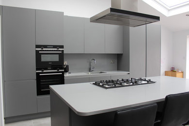 This is an example of a mid-sized modern single-wall eat-in kitchen in London with a single-bowl sink, flat-panel cabinets, quartzite benchtops, grey splashback, glass sheet splashback, stainless steel appliances, with island and grey benchtop.