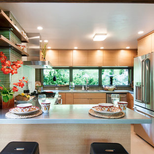 Новый формат декора квартиры: маленькая п-образная кухня-гостиная в стиле ретро с монолитной раковиной, плоскими фасадами, светлыми деревянными фасадами, столешницей из нержавеющей стали, зеленым фартуком, фартуком из стеклянной плитки, техникой из нержавеющей стали, полом из линолеума и полуостровом