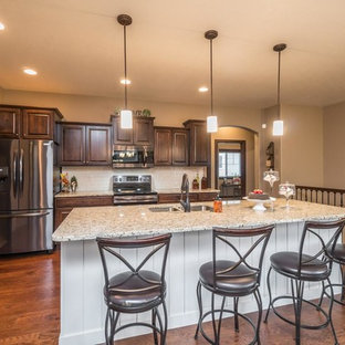 Klassisk inredning av ett mellanstort beige beige kök, med en undermonterad diskho, luckor med upphöjd panel, bruna skåp, granitbänkskiva, beige stänkskydd, stänkskydd i tunnelbanekakel, rostfria vitvaror, mellanmörkt trägolv, en köksö och brunt golv