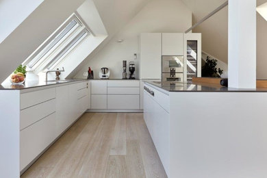 Offene Moderne Küche in L-Form mit flächenbündigen Schrankfronten, weißen Schränken, Granit-Arbeitsplatte, Küchengeräten aus Edelstahl, Kücheninsel und schwarzer Arbeitsplatte in München