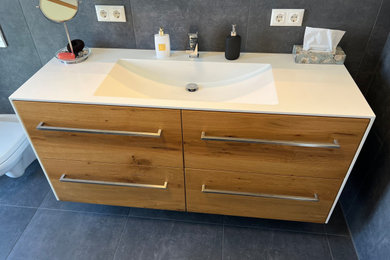 Modernes Badezimmer mit hellbraunen Holzschränken, schwarzen Fliesen, Mineralwerkstoff-Waschtisch, weißer Waschtischplatte, Einzelwaschbecken und schwebendem Waschtisch in Sonstige