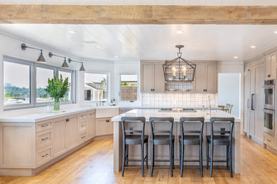 Eat-in kitchen - cottage u-shaped medium tone wood floor and brown floor eat-in kitchen idea in Orange County with a farmhouse sink, shaker cabinets, light wood cabinets, quartz countertops, multicolored backsplash, stainless steel appliances, an island and white countertops