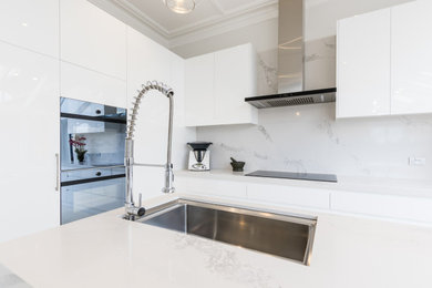 Large contemporary l-shaped kitchen pantry in Melbourne with an undermount sink, flat-panel cabinets, white cabinets, quartz benchtops, engineered quartz splashback, stainless steel appliances, porcelain floors, with island and white benchtop.