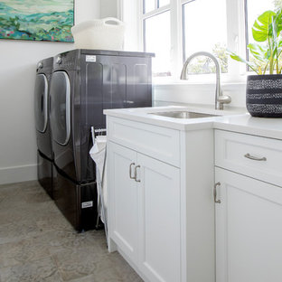 バンクーバーの中サイズのビーチスタイルのおしゃれな洗濯室 (シングルシンク、落し込みパネル扉のキャビネット、白いキャビネット、クオーツストーンカウンター、白い壁、磁器タイルの床、左右配置の洗濯機・乾燥機、ベージュの床、黄色いキッチンカウンター) の写真