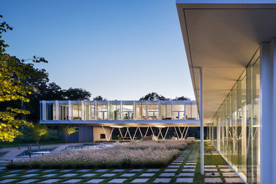 Example of a large minimalist white two-story glass exterior home design in New York with a green roof