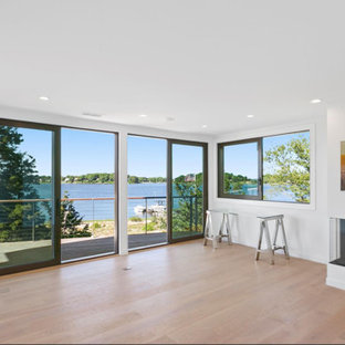Medium sized modern home studio in New York with white walls, light hardwood flooring, a corner fireplace, a plastered fireplace surround, a freestanding desk and beige floors.