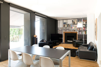Inspiration pour une salle de séjour design de taille moyenne et ouverte avec une bibliothèque ou un coin lecture, un mur noir, parquet clair, une cheminée standard, un manteau de cheminée en bois, un téléviseur indépendant et un sol beige.