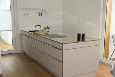 This is an example of a large contemporary galley open plan kitchen in Essen with a drop-in sink, flat-panel cabinets, white cabinets, stainless steel appliances, dark hardwood floors, with island, brown floor, stainless steel benchtops and white splashback.