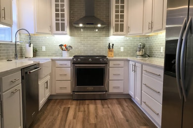 This is an example of a mid-sized country u-shaped separate kitchen in Little Rock with a farmhouse sink, white cabinets, grey splashback, stainless steel appliances, medium hardwood floors, no island, brown floor, shaker cabinets, subway tile splashback and white benchtop.