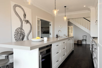 Inspiration for a large beach style galley open plan kitchen in Sydney with a double-bowl sink, flat-panel cabinets, white cabinets, white splashback, subway tile splashback, stainless steel appliances and dark hardwood floors.