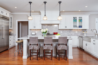 Example of a classic u-shaped medium tone wood floor kitchen design in Boston with a farmhouse sink, beaded inset cabinets, white cabinets, marble countertops, white backsplash, stainless steel appliances, an island and stone slab backsplash