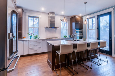 Photo of a large transitional l-shaped eat-in kitchen in Minneapolis with an undermount sink, shaker cabinets, dark wood cabinets, quartz benchtops, white splashback, ceramic splashback, stainless steel appliances, medium hardwood floors, with island and brown floor.