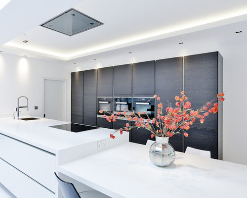This is an example of a modern galley kitchen/diner in London with flat-panel cabinets, dark wood cabinets, black appliances and an island.