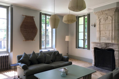 Mittelgroßes, Fernseherloses, Offenes Wohnzimmer mit weißer Wandfarbe, hellem Holzboden, Kamin, Kaminumrandung aus Stein und braunem Boden in Paris