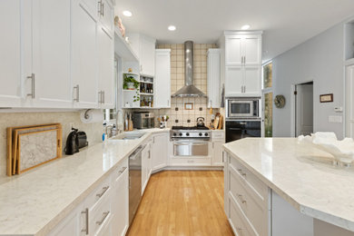Example of a large minimalist u-shaped eat-in kitchen design in San Diego with shaker cabinets, white cabinets, wood countertops, beige backsplash, marble backsplash, stainless steel appliances and white countertops