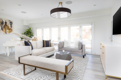 Photo of a transitional living room in Orange County with white walls, light hardwood floors, a wall-mounted tv and grey floor.