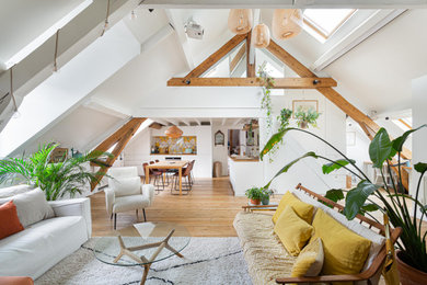 Réalisation d'un grand salon mansardé ou avec mezzanine design avec parquet clair et poutres apparentes.