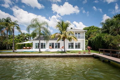 Example of a mid-sized beach style white two-story stucco house exterior design in Tampa with a hip roof and a shingle roof