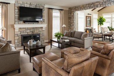 This is an example of a large transitional formal living room in Kansas City with beige walls, medium hardwood floors, a standard fireplace, a stone fireplace surround, a wall-mounted tv and brown floor.