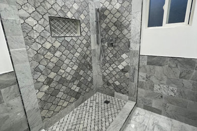 Modelo de cuarto de baño doble de estilo americano de tamaño medio con puertas de armario grises, aseo y ducha, encimera de granito, ducha esquinera, sanitario de una pieza, baldosas y/o azulejos grises, baldosas y/o azulejos de mármol, paredes blancas, ducha con puerta con bisagras y encimeras grises