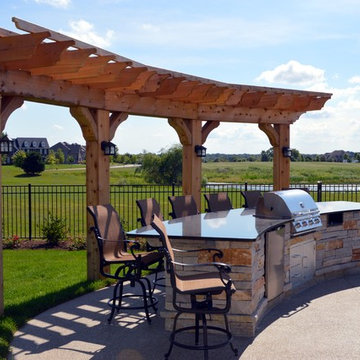 Free form pool with stone table, sun shelf, water feature, and outdoor kitchen,