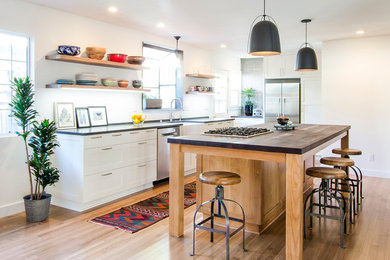 Photo of a contemporary u-shaped kitchen in Santa Barbara with a farmhouse sink, white cabinets, white splashback, stainless steel appliances, light hardwood floors, with island and shaker cabinets.