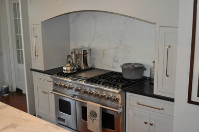 Example of a large transitional u-shaped medium tone wood floor eat-in kitchen design in Atlanta with a farmhouse sink, recessed-panel cabinets, white cabinets, marble countertops, white backsplash, subway tile backsplash, stainless steel appliances and an island