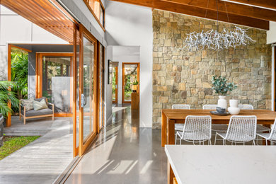 На фото: гостиная-столовая среднего размера в современном стиле с коричневыми стенами, бетонным полом, серым полом, балками на потолке и панелями на стенах с
