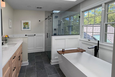 Inspiration for a large transitional master white tile and porcelain tile porcelain tile, gray floor, double-sink, vaulted ceiling and wainscoting bathroom remodel in Philadelphia with light wood cabinets, a one-piece toilet, beige walls, an undermount sink, quartz countertops, a hinged shower door and white countertops