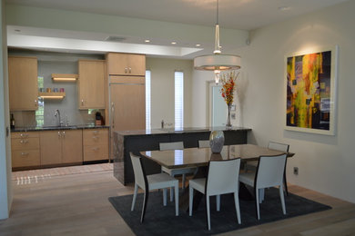 This is an example of a large contemporary galley eat-in kitchen in Phoenix with an undermount sink, flat-panel cabinets, light wood cabinets, panelled appliances, granite benchtops, white splashback, stone slab splashback, light hardwood floors and a peninsula.