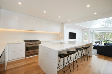 Design ideas for a mid-sized modern galley eat-in kitchen in Sydney with an undermount sink, flat-panel cabinets, white cabinets, marble benchtops, white splashback, light hardwood floors, with island and white benchtop.