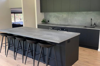 Mid-sized contemporary galley kitchen in Melbourne with flat-panel cabinets, black cabinets, quartz benchtops, grey splashback, engineered quartz splashback, black appliances, with island and grey benchtop.