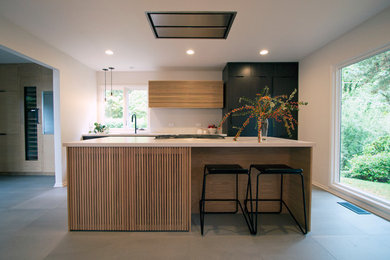 This is an example of a mid-sized midcentury single-wall eat-in kitchen in Portland with an undermount sink, flat-panel cabinets, dark wood cabinets, quartz benchtops, white splashback, black appliances, porcelain floors, with island and grey floor.