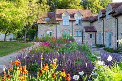 Imagen de jardín de estilo de casa de campo grande en verano en patio trasero con jardín francés, parterre de flores y adoquines de piedra natural
