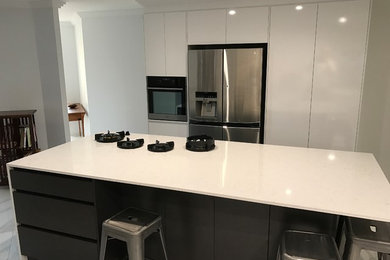 This is an example of a mid-sized modern eat-in kitchen in Brisbane with a single-bowl sink, white cabinets, quartz benchtops, black appliances, porcelain floors, with island and multi-coloured floor.
