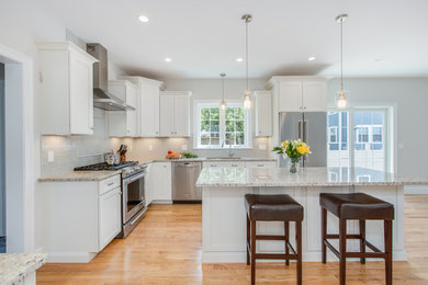 Inspiration for a large transitional l-shaped open plan kitchen in Boston with an undermount sink, shaker cabinets, white cabinets, granite benchtops, grey splashback, subway tile splashback, stainless steel appliances, light hardwood floors and with island.