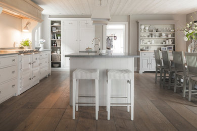 Design ideas for a mid-sized traditional single-wall open plan kitchen in Munich with beaded inset cabinets, wood benchtops, painted wood floors, with island, a drop-in sink, white cabinets, grey splashback, glass sheet splashback, stainless steel appliances and brown floor.
