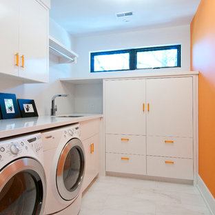 Medium sized contemporary l-shaped separated utility room in Toronto with flat-panel cabinets, white cabinets, a side by side washer and dryer, a submerged sink, engineered stone countertops, orange walls, porcelain flooring and white worktops.
