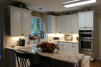 Open concept kitchen - mid-sized l-shaped medium tone wood floor open concept kitchen idea in Atlanta with a single-bowl sink, raised-panel cabinets, white cabinets, granite countertops, beige backsplash, subway tile backsplash, stainless steel appliances and an island