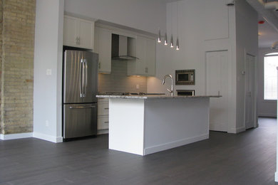 Inspiration for a contemporary medium tone wood floor kitchen remodel in Toronto with a double-bowl sink, recessed-panel cabinets, white cabinets, granite countertops, white backsplash, subway tile backsplash, stainless steel appliances and an island