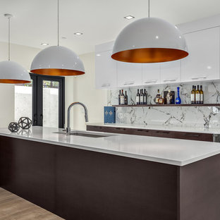 バンクーバーの中サイズのコンテンポラリースタイルのおしゃれな着席型バー (アンダーカウンターシンク、フラットパネル扉のキャビネット、濃色木目調キャビネット、クオーツストーンカウンター、白いキッチンパネル、磁器タイルのキッチンパネル、淡色無垢フローリング、茶色い床、白いキッチンカウンター) の写真