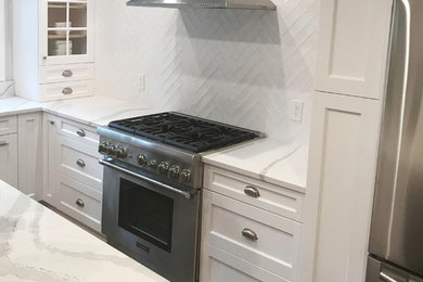 Large transitional l-shaped dark wood floor and brown floor enclosed kitchen photo in New York with an undermount sink, recessed-panel cabinets, white cabinets, marble countertops, white backsplash, ceramic backsplash, stainless steel appliances and an island