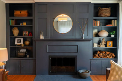 Diseño de biblioteca en casa abierta de estilo americano de tamaño medio con paredes azules, suelo de madera clara y marco de chimenea de madera
