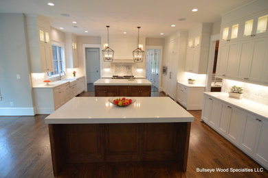 Photo of an expansive classic u-shaped open plan kitchen in DC Metro with a belfast sink, shaker cabinets, medium wood cabinets, engineered stone countertops, white splashback, integrated appliances, medium hardwood flooring, multiple islands, brown floors and white worktops.