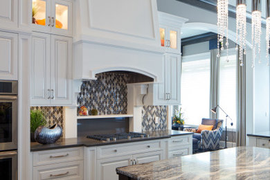 Large transitional medium tone wood floor and brown floor kitchen photo in Omaha with an undermount sink, raised-panel cabinets, white cabinets, granite countertops, multicolored backsplash, mosaic tile backsplash, paneled appliances, two islands and gray countertops