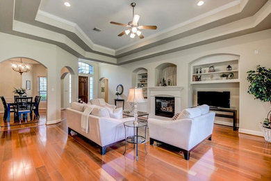 Mid-sized transitional open concept medium tone wood floor family room photo in Houston with gray walls, a standard fireplace, a plaster fireplace and a tv stand